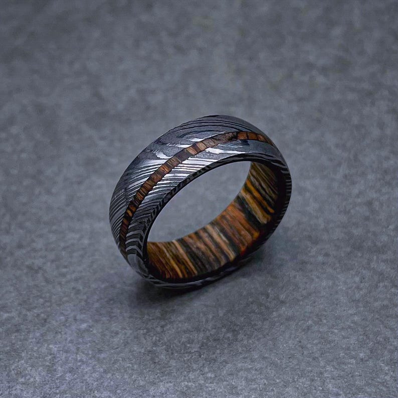 May include: A silver and brown patterned metal ring with a wide band.