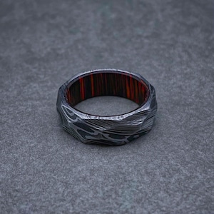 May include: A silver ring with a textured, patterned surface and a red and black wood inlay.