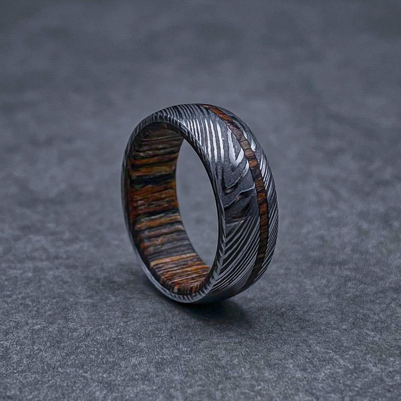 May include: A silver and brown patterned metal ring with a thin band of wood.