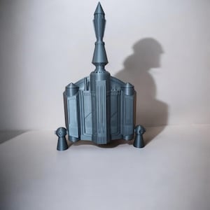 Puede incluir: Un modelo de nave espacial impreso en 3D con una parte superior puntiaguda y dos alas laterales. El modelo está pintado en color plateado.