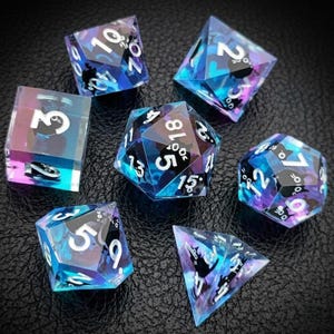 May include: Set of seven polyhedral dice with a blue and purple iridescent effect. Each die features white numbers and black cat silhouettes. The dice are designed for tabletop role-playing games.