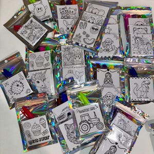 May include: A collection of small, clear, iridescent zipper bags, each containing a coloring page and a crayon. The coloring pages feature various black and white illustrations of animals, sweets, and other fun designs. Some bags have the text "LIFE IS SWEET" and "COUNTRY LIFE".
