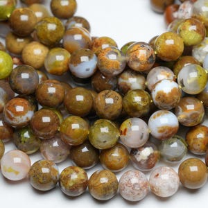 Peut inclure: Un brin de perles rondes en agate de couleur marron, verte et blanche. Les perles ont un aspect marbré et moucheté.