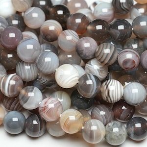 Peut inclure: Un brin de perles d'agate grises, blanches et brunes. Les perles sont rondes et ont une finition polie. Les perles sont de tailles différentes et présentent des motifs uniques.