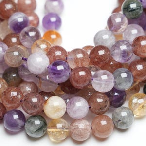 May include: A strand of round, multi-coloured gemstone beads. The beads are a mix of purple, pink, brown, and clear with flecks of gold and silver. The beads are approximately 10mm in diameter.