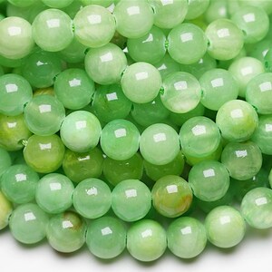 Peut inclure: Gros plan sur une collection de perles rondes vert clair. Les perles ont une surface lisse et polie et varient légèrement de teinte, du pâle au vert plus foncé. Ces perles sont enfilées, ce qui suggère qu'elles sont destinées à la fabrication de bijoux.
