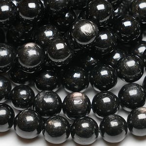 Puede incluir: Una hebra de cuentas de obsidiana negra con un efecto brillante e iridiscente. Las cuentas son redondas y lisas, y están enhebradas en un hilo transparente.