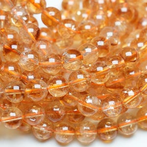 Op de afbeelding: Een streng ronde, doorschijnende, amberkleurige kralen met een lichte oranje tint. De kralen zijn glad en gepolijst, met een lichte glans.