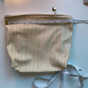 May include: A beige and white striped cosmetic bag with a gold zipper and pull. The bag is approximately 12 inches long. A white measuring tape is next to the bag.