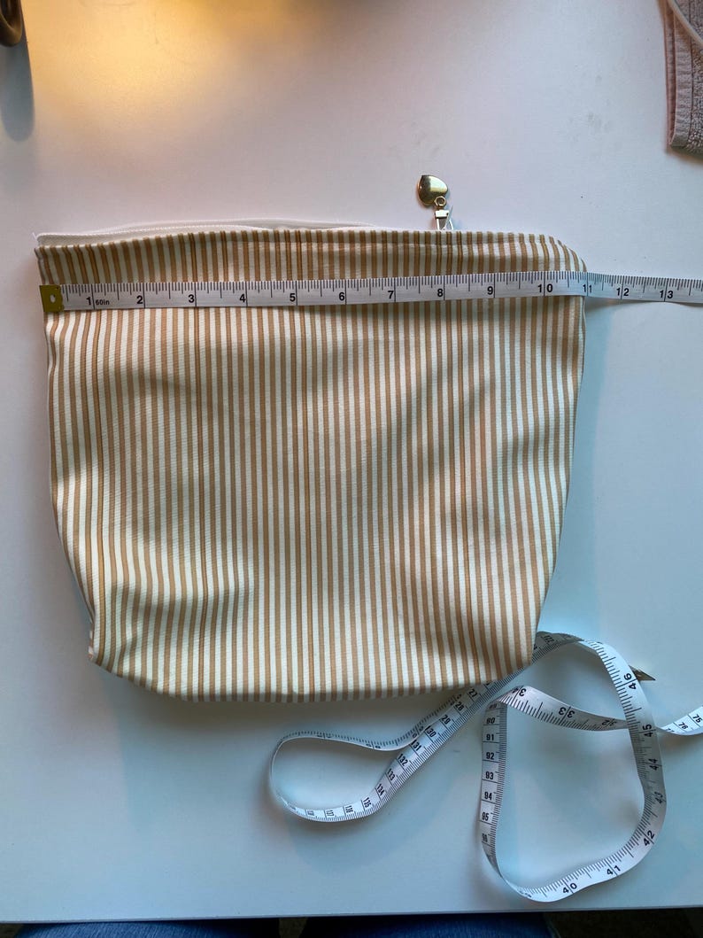 May include: A beige and white striped cosmetic bag with a gold zipper and pull. The bag is approximately 12 inches long. A white measuring tape is next to the bag.