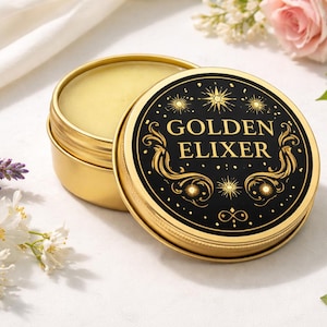 May include: A gold tin with a black lid, displaying "GOLDEN ELIXER" in gold lettering. The open tin reveals a yellow balm. The lid has a decorative design with stars and swirls. Flowers and herbs are arranged around the tin, creating a natural aesthetic.