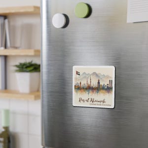 May include: A square magnet featuring a watercolor illustration of the Ras al Khaimah skyline in the United Arab Emirates. The design includes the UAE flag, mountains, and the text "Ras al Khaimah, United Arab Emirates."