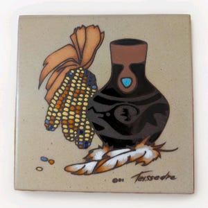 Puede incluir: Azulejo cerámico cuadrado con diseño nativo americano. La obra representa un jarrón negro con un acento turquesa, una mazorca de maíz y plumas. El azulejo tiene un fondo beige y la firma del artista.