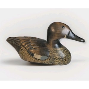 May include: A wooden duck figurine with a detailed carved design. The duck has a brown body with lighter brown and gray accents on the wings and chest. The beak is black, and the eye is a small black dot.