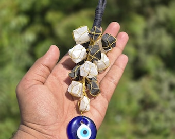 May include: A white and black crystal charm with a gold wire cage and a blue evil eye charm hanging from a black cord.