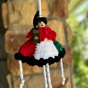 May include: A handmade doll with a red, white, black, and green dress. The doll has a wooden head with painted features and a black hat. A tag that says "Made with LOVE" hangs from the doll.