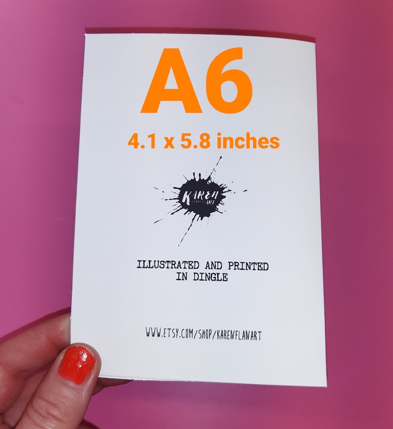 May include: A white card with the text "A6 4.1 x 5.8 inches" printed in orange. The card also has a black ink splatter with the text "Kireh" in white. The text "Illustrated and printed in Dingle" and "www.etsy.com/shop/karewflanart" are also printed on the card.