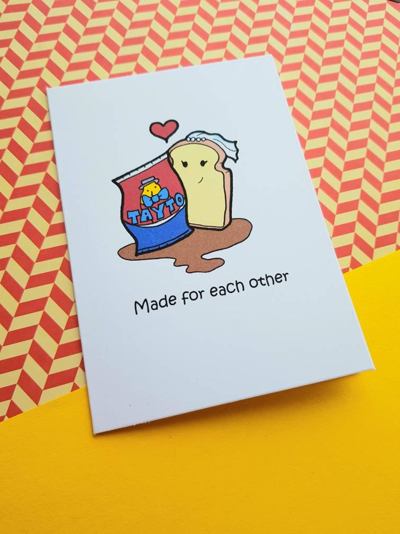 Peut inclure: Une carte blanche avec une illustration de dessin anim&eacute; d'un sac de chips Tayto et une tranche de pain avec un c&oelig;ur au-dessus. Le texte "Made for each other" est sous l'illustration.
