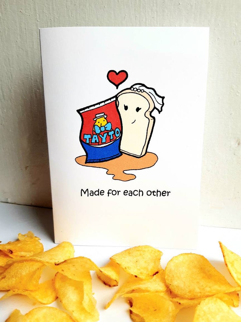Peut inclure: Une carte de v&oelig;ux avec une illustration de dessin anim&eacute; d'un sac de chips Tayto et une tranche de pain avec un voile. Le texte sur la carte dit "Made for each other".