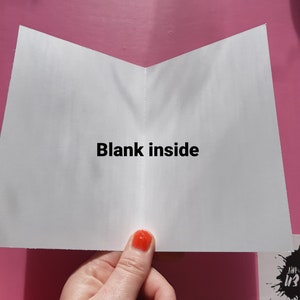 May include: A white card with the text "Blank inside" printed in black. The card is folded in half and is being held by a hand.