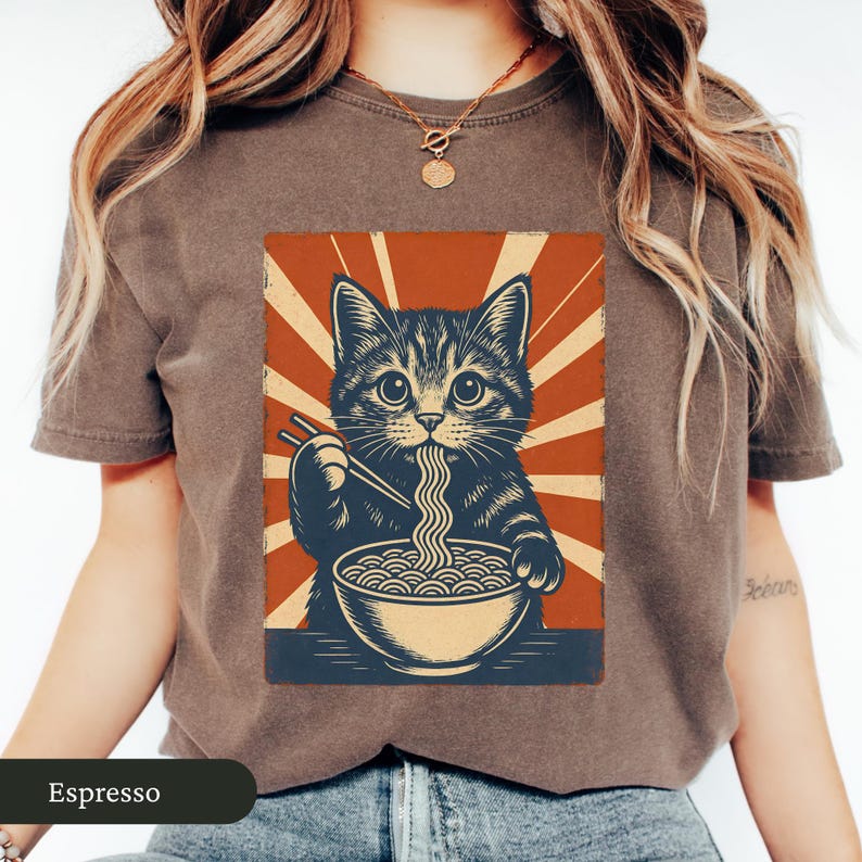May include: Espresso-colored t-shirt featuring a graphic of a cat eating ramen noodles. The cat illustration is in a vintage style with a red and cream background. The text "Espresso" is at the bottom of the shirt.