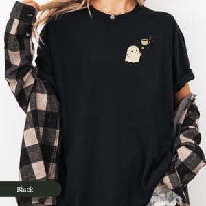 May include: Black t-shirt featuring a small cartoon ghost with a coffee cup and star design. The shirt has a crew neck and long sleeves. The word "Black" is displayed on a dark green bar at the bottom left of the image.