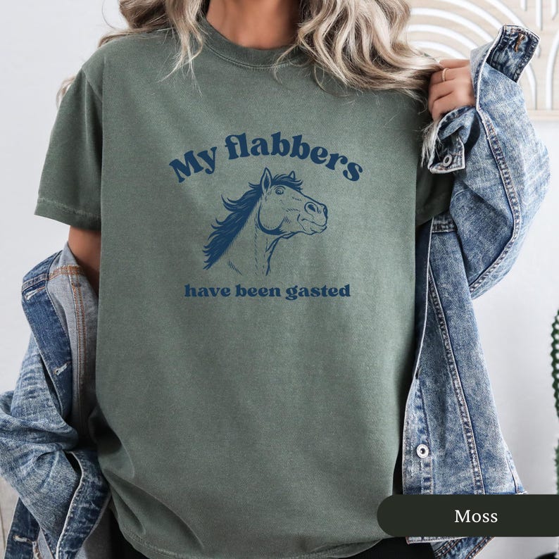 May include: Moss green t-shirt with the text "My flabbers have been gasted" and a blue horse illustration. The shirt is a crew neck style and has short sleeves. The shirt is made of a soft material.