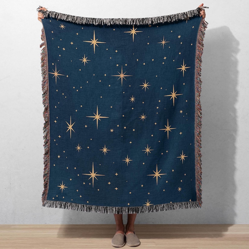 Puede incluir: Una manta azul marino con un patr&oacute;n repetido de estrellas doradas. La manta tiene un borde con flecos en tonos marrones y beige. Las estrellas var&iacute;an en tama&ntilde;o y est&aacute;n espaciadas uniformemente sobre la superficie de la manta.