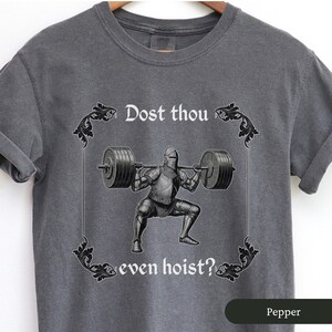 Pode incluir: Uma camiseta cinza com um gr&aacute;fico de estilo medieval de um cavaleiro levantando pesos. O texto na camiseta diz "Dost thou even hoist?"