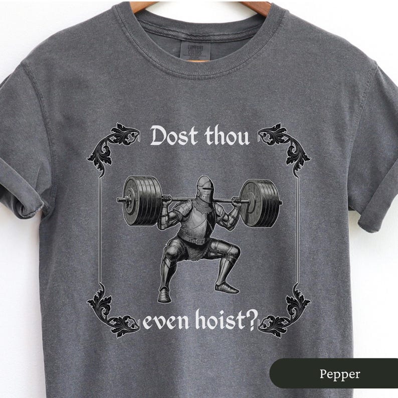 Pode incluir: Uma camiseta cinza com um gr&aacute;fico de estilo medieval de um cavaleiro levantando pesos. O texto na camiseta diz "Dost thou even hoist?"