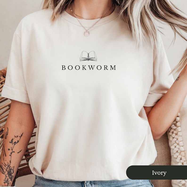 Op de afbeelding: Ivoor kleurig T-shirt met de zwarte tekst "BOOKWORM" en een lijntekening van een open boek. Het T-shirt heeft een ronde hals en korte mouwen. De stof lijkt zacht en comfortabel.