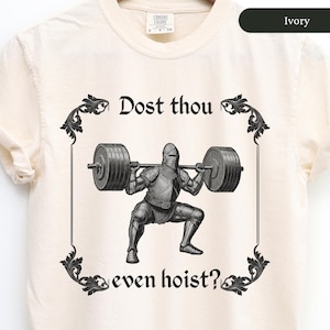 Peut inclure: Un t-shirt blanc avec une illustration en noir et blanc d'un chevalier soulevant des poids. Le texte "Dost thou even hoist?" est imprimé sur le t-shirt.