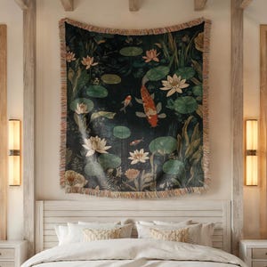 K&ouml;nnte beinhalten: Ein gewebtes Wandbehang mit einer Koi-Teich-Szene mit orangefarbenen und wei&szlig;en Fischen, Seerosen und Lotusblumen. Der Wandbehang hat einen dunkelgr&uuml;nen Hintergrund und einen Fransenrand. Er h&auml;ngt &uuml;ber einem Bett mit wei&szlig;er Bettw&auml;sche.