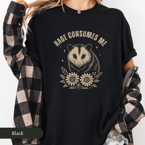 May include: Black t-shirt with a possum illustration and the text "Rage Consumes Me." The possum is framed by flowers. A casual, comfortable style of shirt.