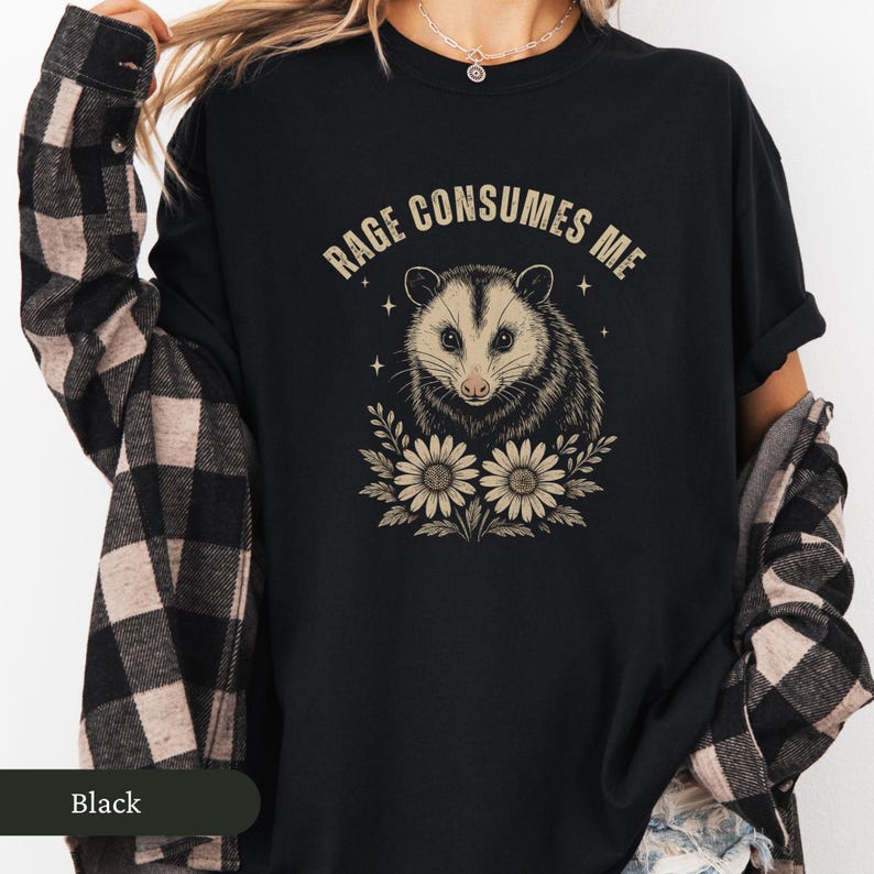 May include: Black t-shirt with a possum illustration and the text "Rage Consumes Me." The possum is framed by flowers. A casual, comfortable style of shirt.