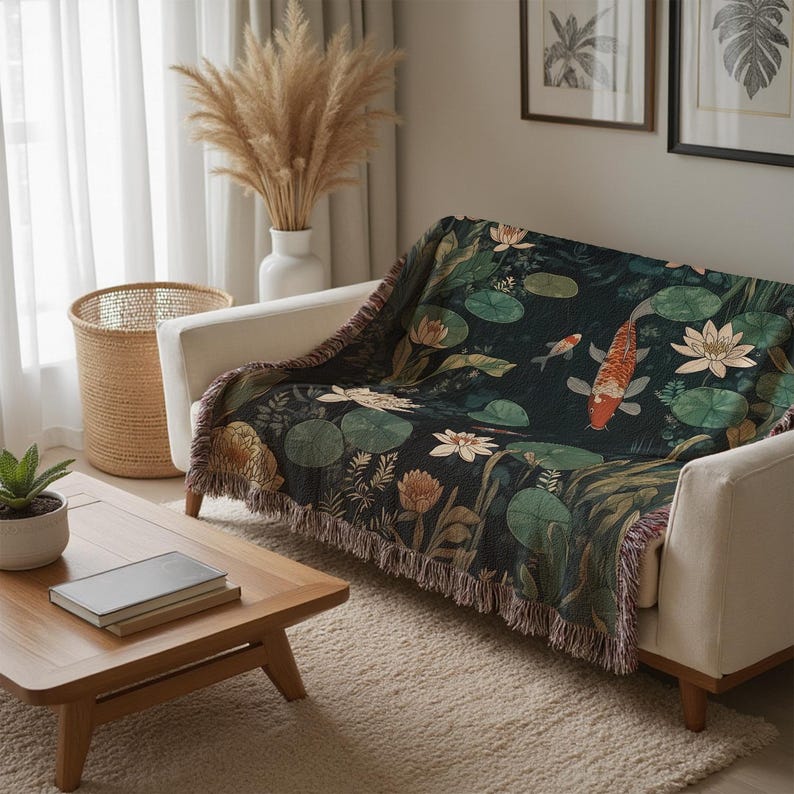 K&ouml;nnte beinhalten: Eine dekorative Tagesdecke mit einem Koi-Teich-Design, das orange und wei&szlig;e Fische, Seerosen und Blumen auf einem dunkelgr&uuml;nen Hintergrund zeigt. Die Decke hat einen Fransenrand und ist &uuml;ber ein wei&szlig;es Sofa drapiert.