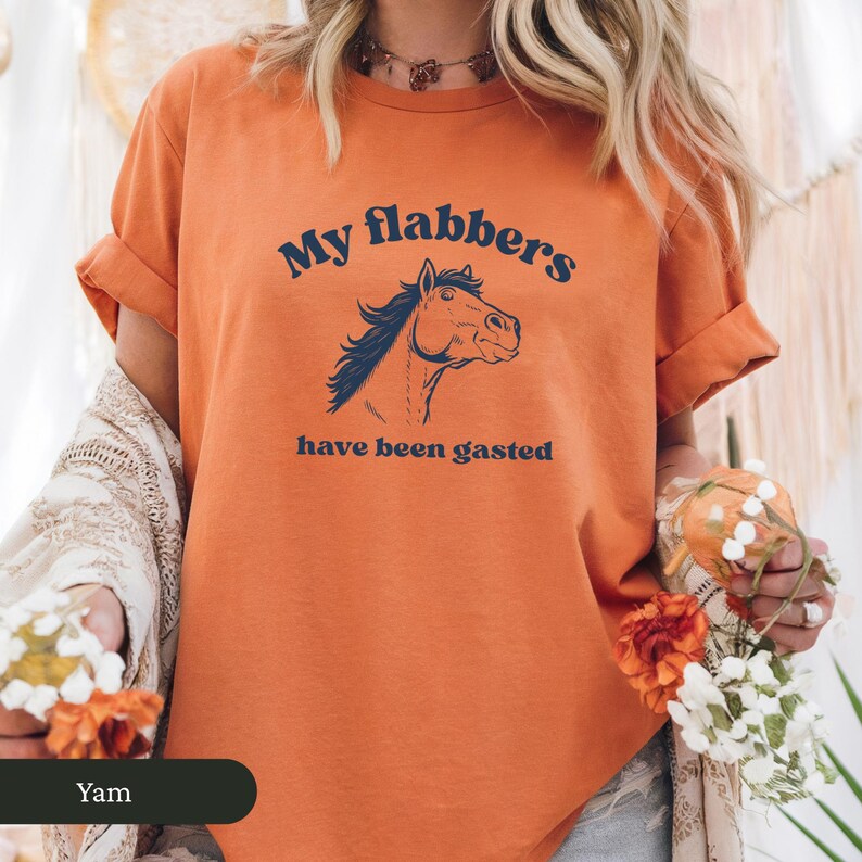 May include: Orange t-shirt with rolled-up sleeves featuring a horse head graphic and the text "My flabbers have been gasted" in navy blue. The shirt is a casual wear item.