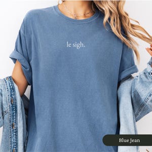 Pu&ograve; includere: Una maglietta blu jeans con la scritta "le sigh" in bianco. La maglietta ha le maniche arrotolate e una vestibilit&agrave; rilassata. La maglietta &egrave; realizzata in un materiale morbido.
