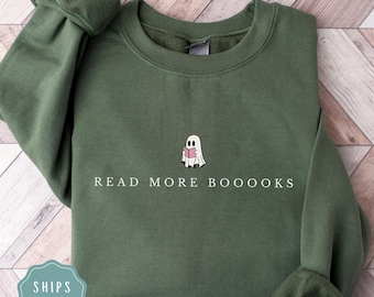 May include: Military green sweatshirt with the text "READ MORE BOOOOKS" and a small ghost graphic holding a pink book. The sweatshirt is a solid color and has a crew neck.