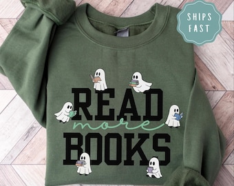 May include: Olive green sweatshirt with the words "READ more BOOKS" in black block letters and a light green cursive font. The design includes cartoon ghosts holding books. The sweatshirt has long sleeves.