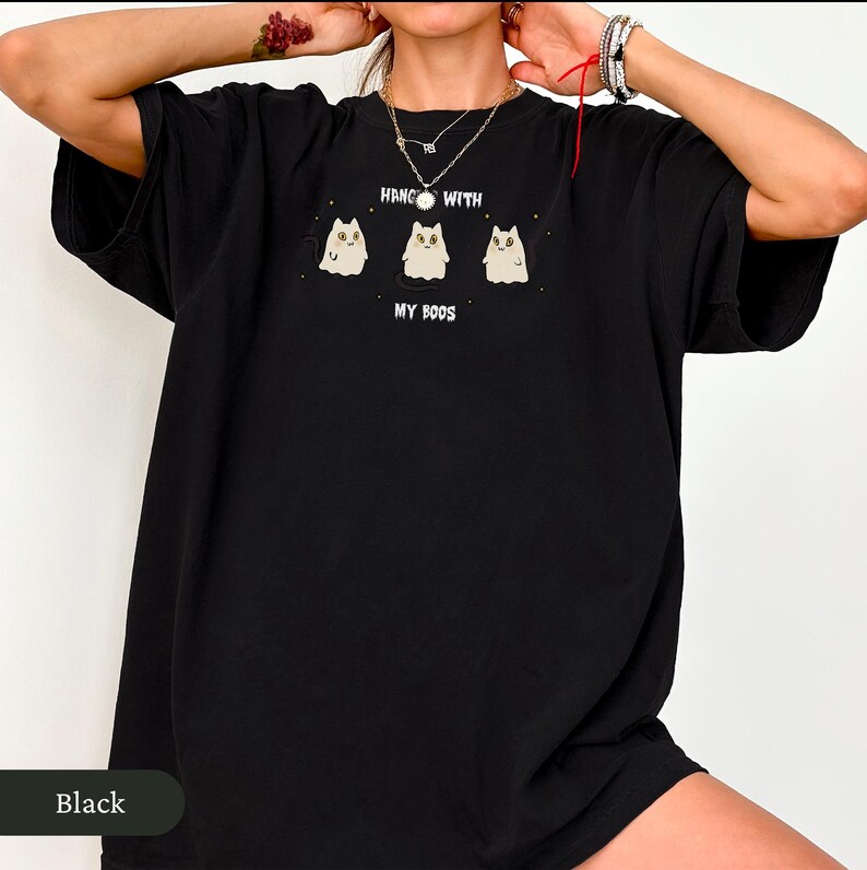 May include: Black t-shirt with a graphic of three cartoon ghosts with cat-like features. The text "HANG WITH MY BOOS" is printed above the ghosts. The shirt is a casual, oversized style.