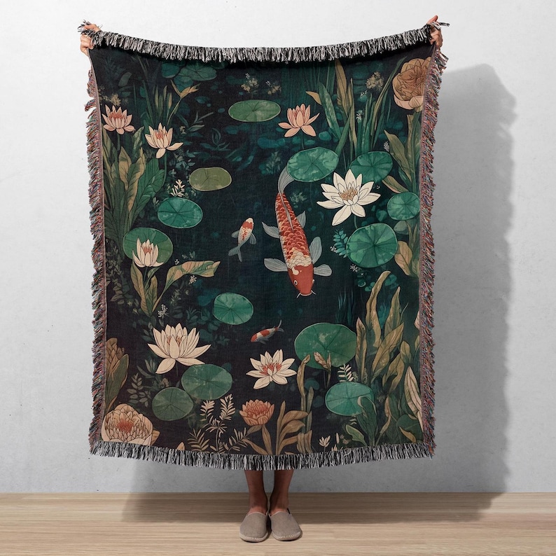 K&ouml;nnte beinhalten: Eine gewebte Wurmdecke mit einer dunkelgr&uuml;nen Teichszene mit Koi-Karpfen, Seerosen und Lotusblumen. Die Decke hat einen Fransenrand mit Braun- und Beiget&ouml;nen. Die Koi-Karpfen sind orange und wei&szlig;.