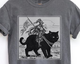May include: Dark gray t-shirt featuring a black and white illustration of a knight in armor riding a large black cat. The knight holds a flag and spear. The shirt has a Pepper color label.