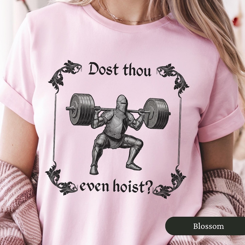 Pode incluir: Camiseta rosa com um gr&aacute;fico de um cavaleiro de armadura levantando pesos. O texto na camiseta diz "Dost thou even hoist?"