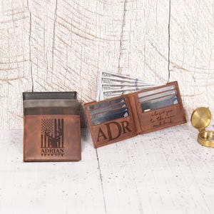 May include: Leather wallets in shades of brown and gray are displayed, one open to reveal card slots and the initials "ADR". Another wallet features a deer silhouette and the text "ADRIAN". A compass and cash are also visible.