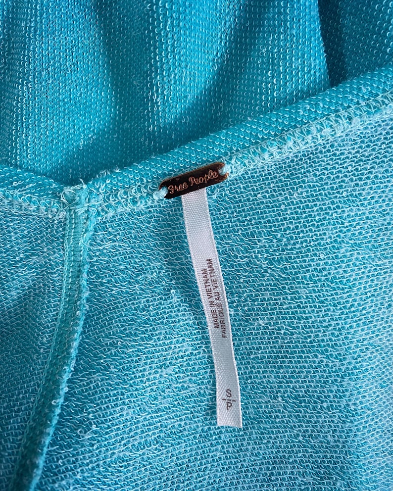May include: A turquoise blue garment tag with the text "Free People" and "Made in Vietnam / Fabrique au Vietnam" printed on it.
