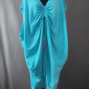 May include: A turquoise blue, loose-fitting, sleeveless top with a drawstring neckline.