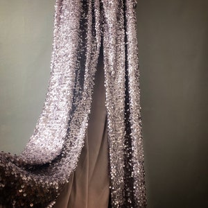 May include: A pair of silver sequined pants hanging on a wall. The pants are made of a soft, flowing fabric and have a relaxed fit.