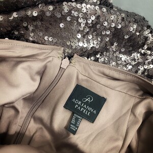May include: A brown dress with a zipper closure and a black label that reads "Adrianna Papell". The label also includes size information in US, EU, UK, GER, and AUS sizes. The dress is made in China.