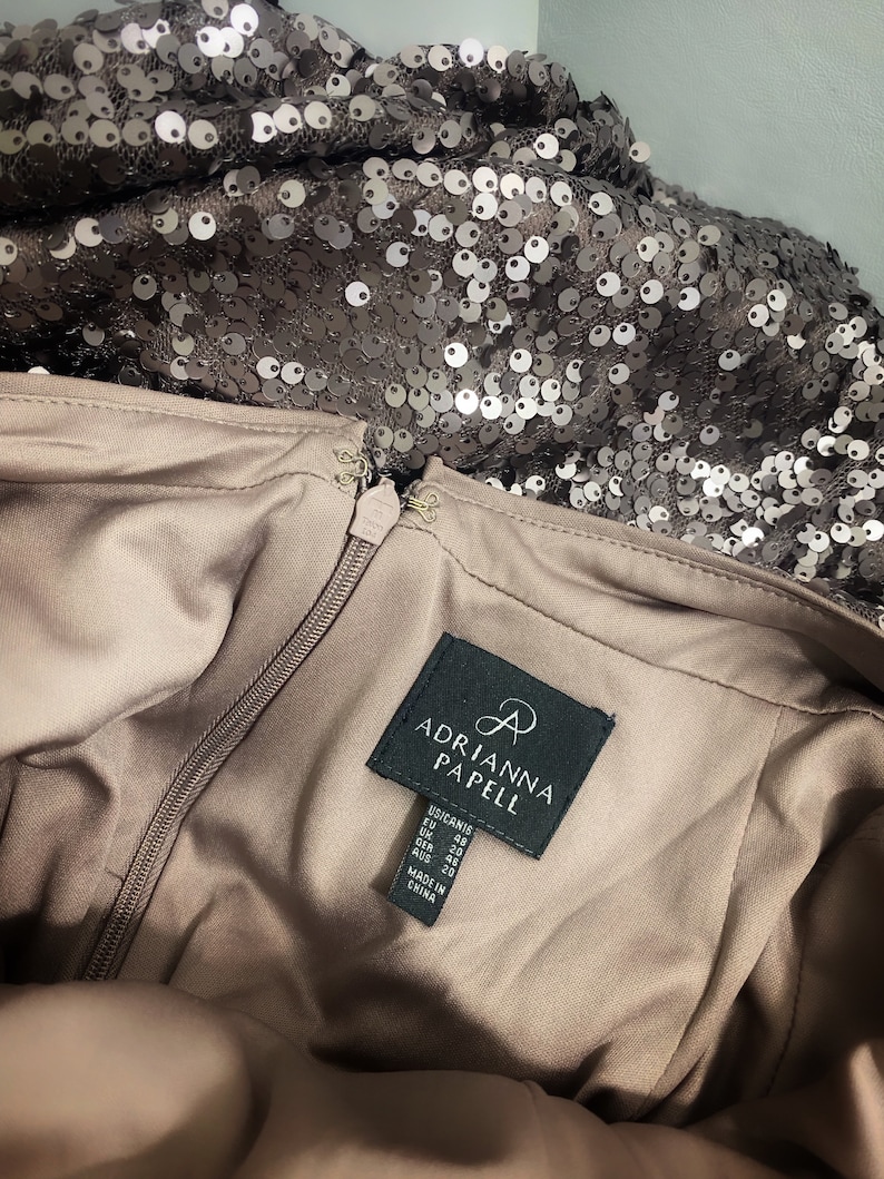 May include: A brown dress with a zipper closure and a black label that reads "Adrianna Papell". The label also includes size information in US, EU, UK, GER, and AUS sizes. The dress is made in China.